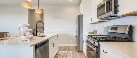 A modern kitchen with white cabinetry, stainless steel appliances, and pendant lighting.