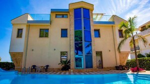 A modern hotel with a swimming pool, a glass elevator, and a palm tree. - Apartments in Villa Fortunata (Terracina)