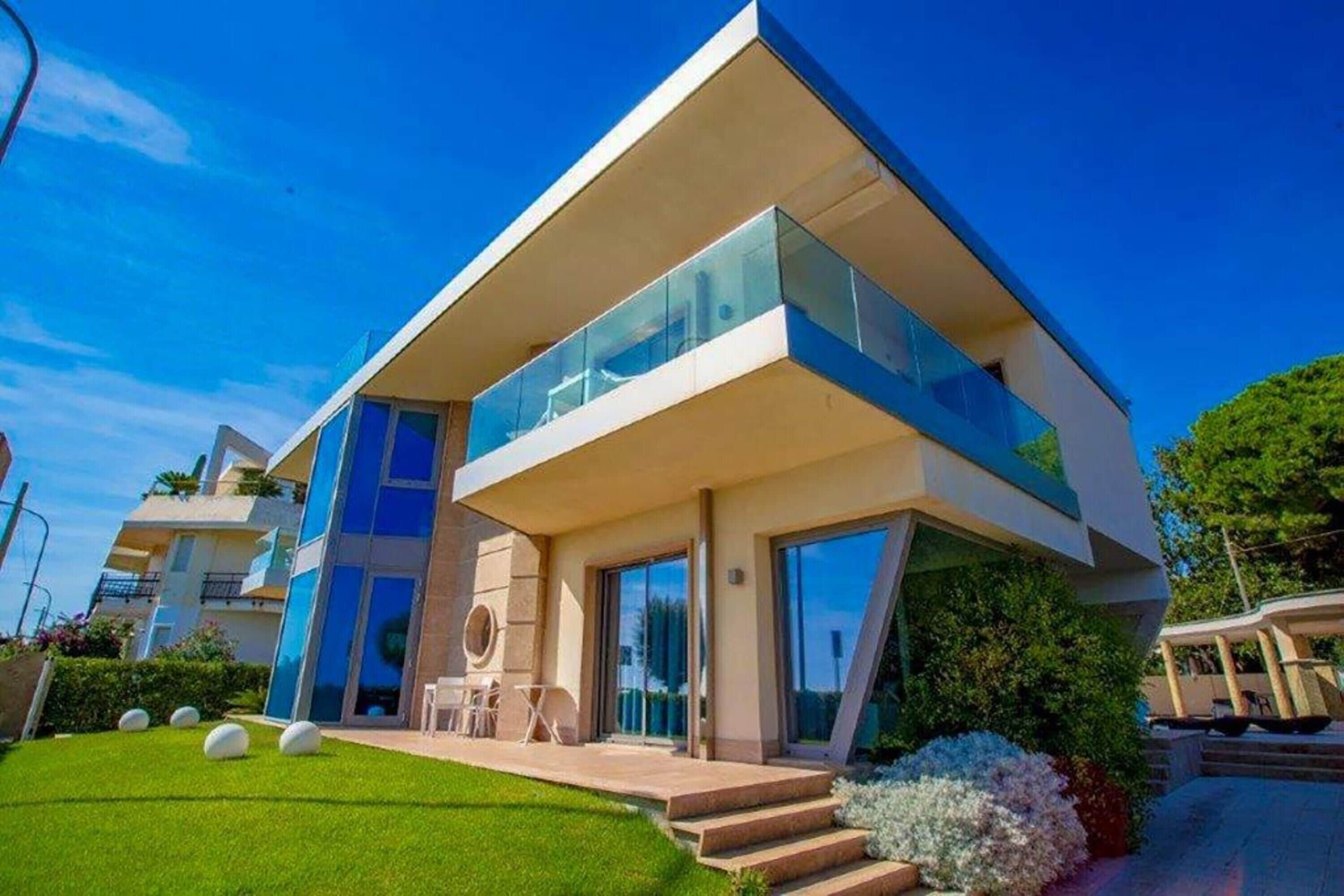 A modern two-story house with a flat roof, large glass windows, and a well-maintained lawn.
