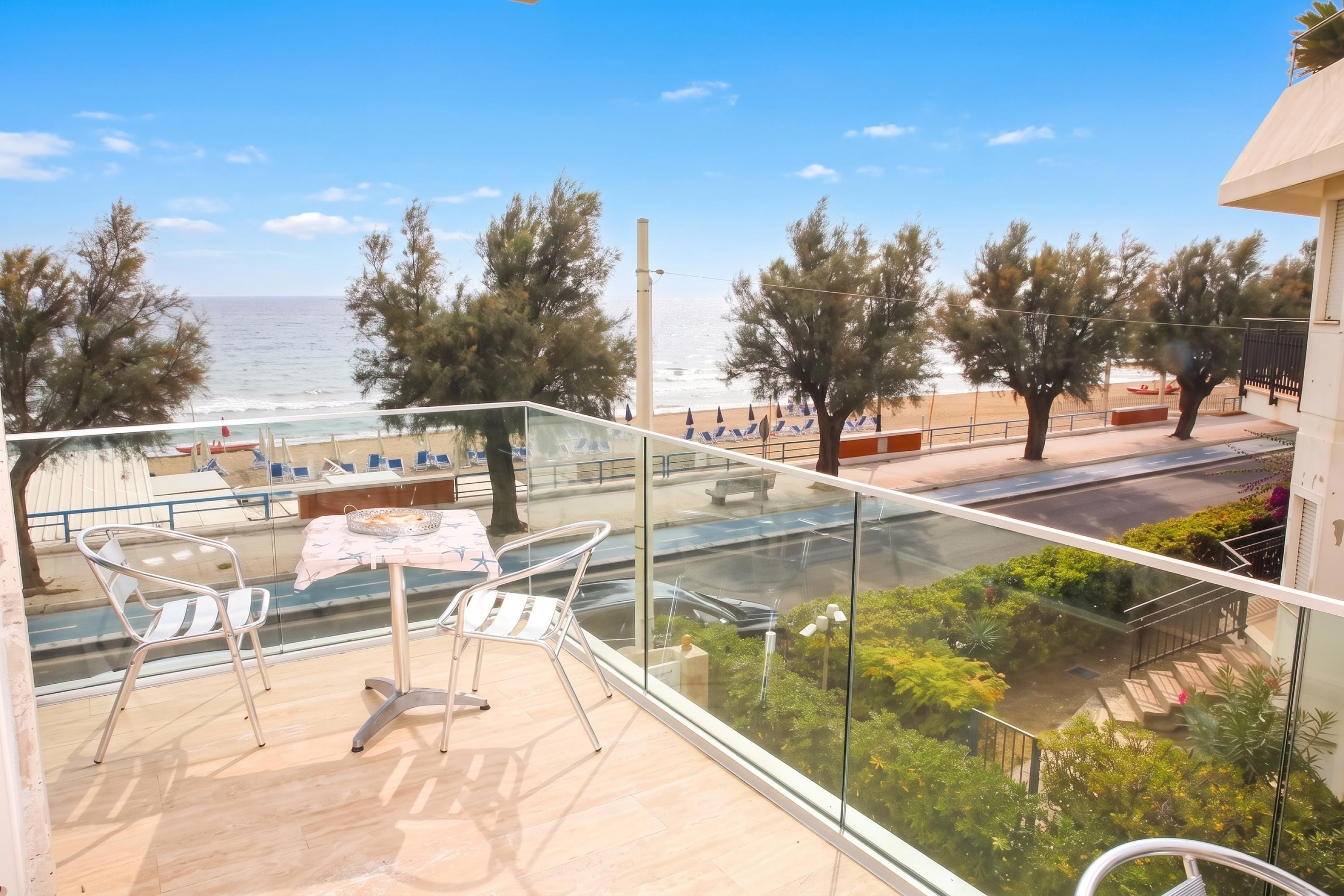 A balcony with a view of the beach, a table with chairs, and a glass railing.