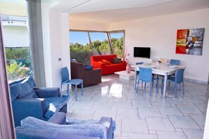 A modern living room with a dining area, large windows, and a flat-screen TV. - Apartments in Villa Fortunata (Terracina)