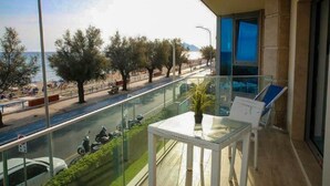 A balcony with a glass railing overlooking a beach and road. There is a table with a potted plant and two chairs. - Apartments in Villa Fortunata (Terracina)