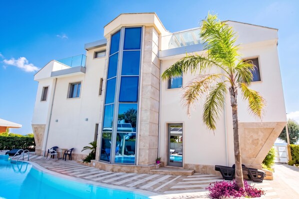 A modern two-story building with a swimming pool, large windows, and a palm tree. - Apartments in Villa Fortunata (Terracina)