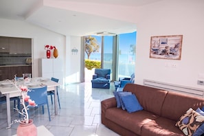 A modern living room with a brown sofa, a dining area with a white table, and a kitchen with wooden cabinets. - Apartments in Villa Fortunata (Terracina)