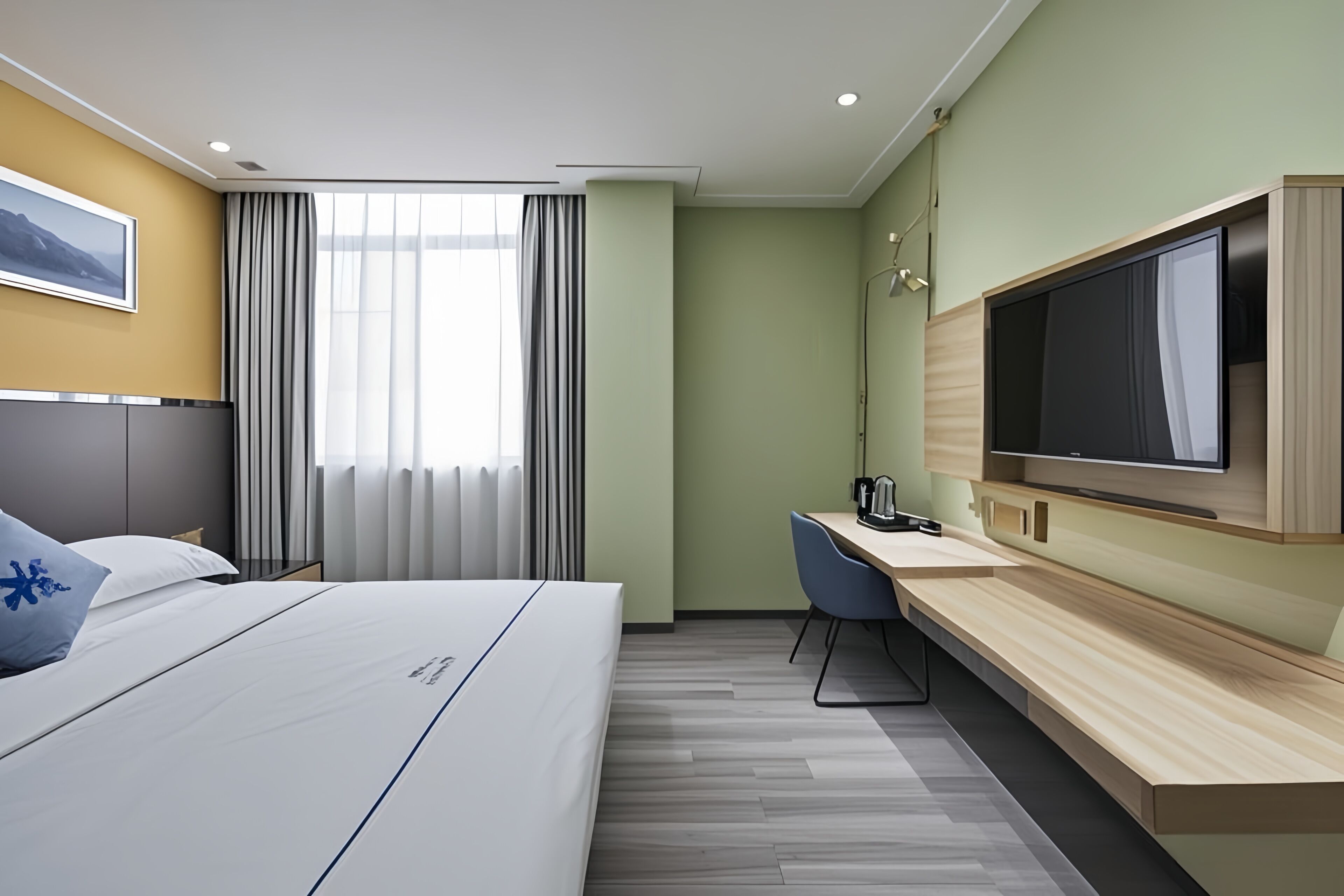 Ein Hotelzimmer mit Bett, Schreibtisch, Stuhl, Fernseher und einem Fenster mit Vorhängen.