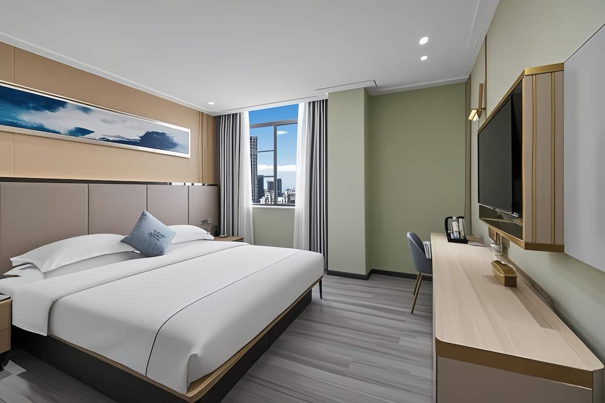 Ein modernes Hotelzimmer mit einem großen Bett, einem Schreibtisch, einem Fernseher und Blick auf die Stadt durch das Fenster.