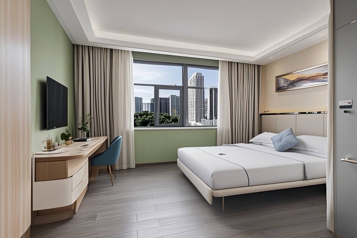 Ein modernes Hotelzimmer mit großem Fenster, Schreibtisch, Bett und Fernseher.