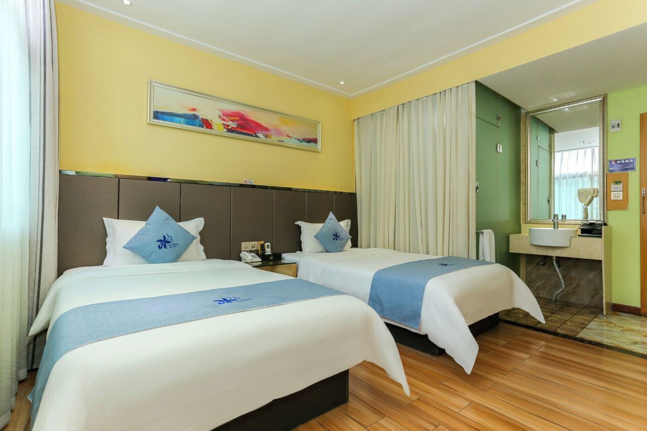 A hotel room with two beds, a large mirror, a painting on the wall, and a bathroom with a sink and mirror.