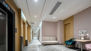 A modern hotel corridor with a marble floor, a sofa, a teal chair, and a small table with a vase. - AeroLink Hotel Shenzhen Bao'an Airport  (Shenzhen)