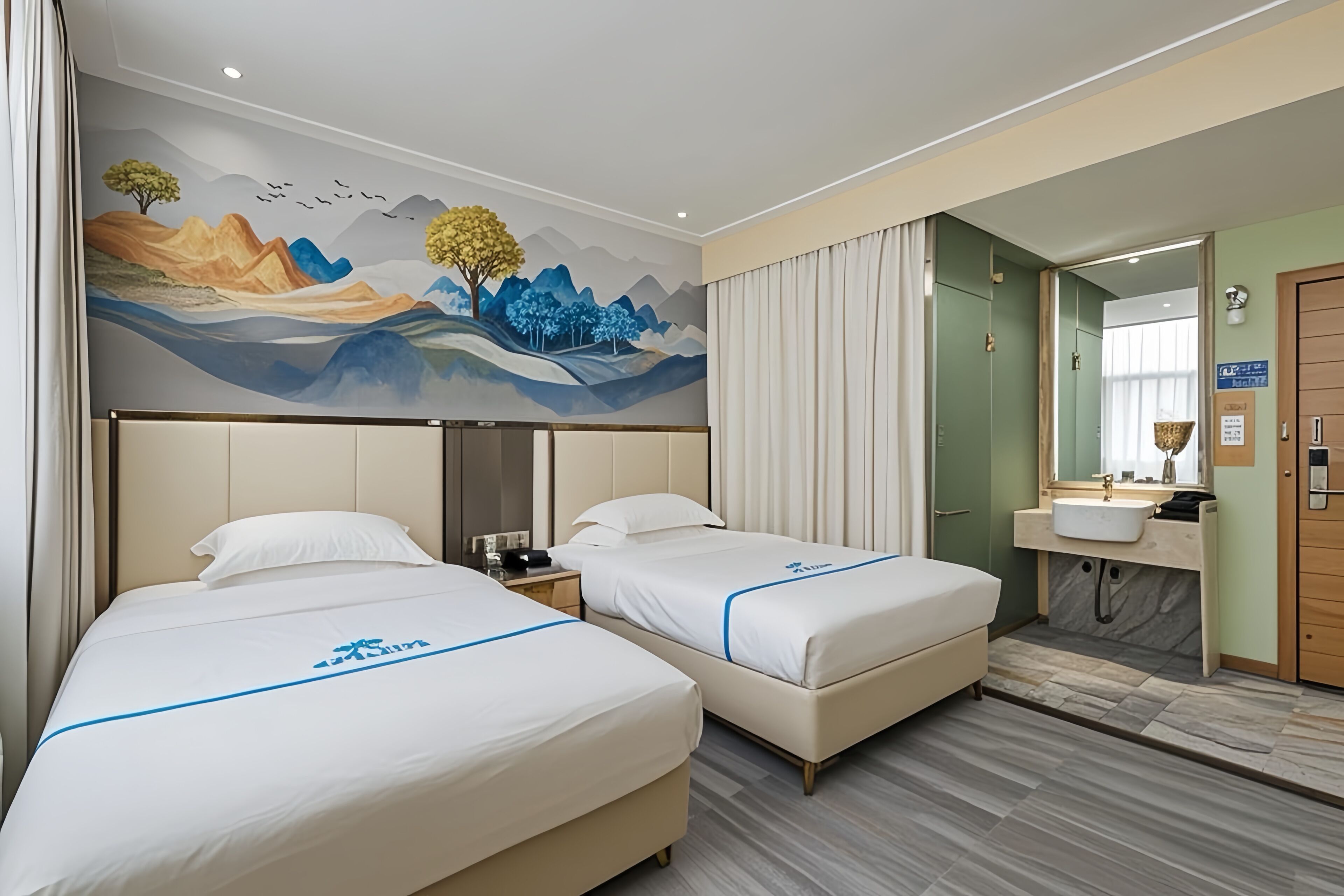 Une chambre d’hôtel avec deux lits, une fresque murale, une salle de bain avec un lavabo et un miroir, et une porte en bois.