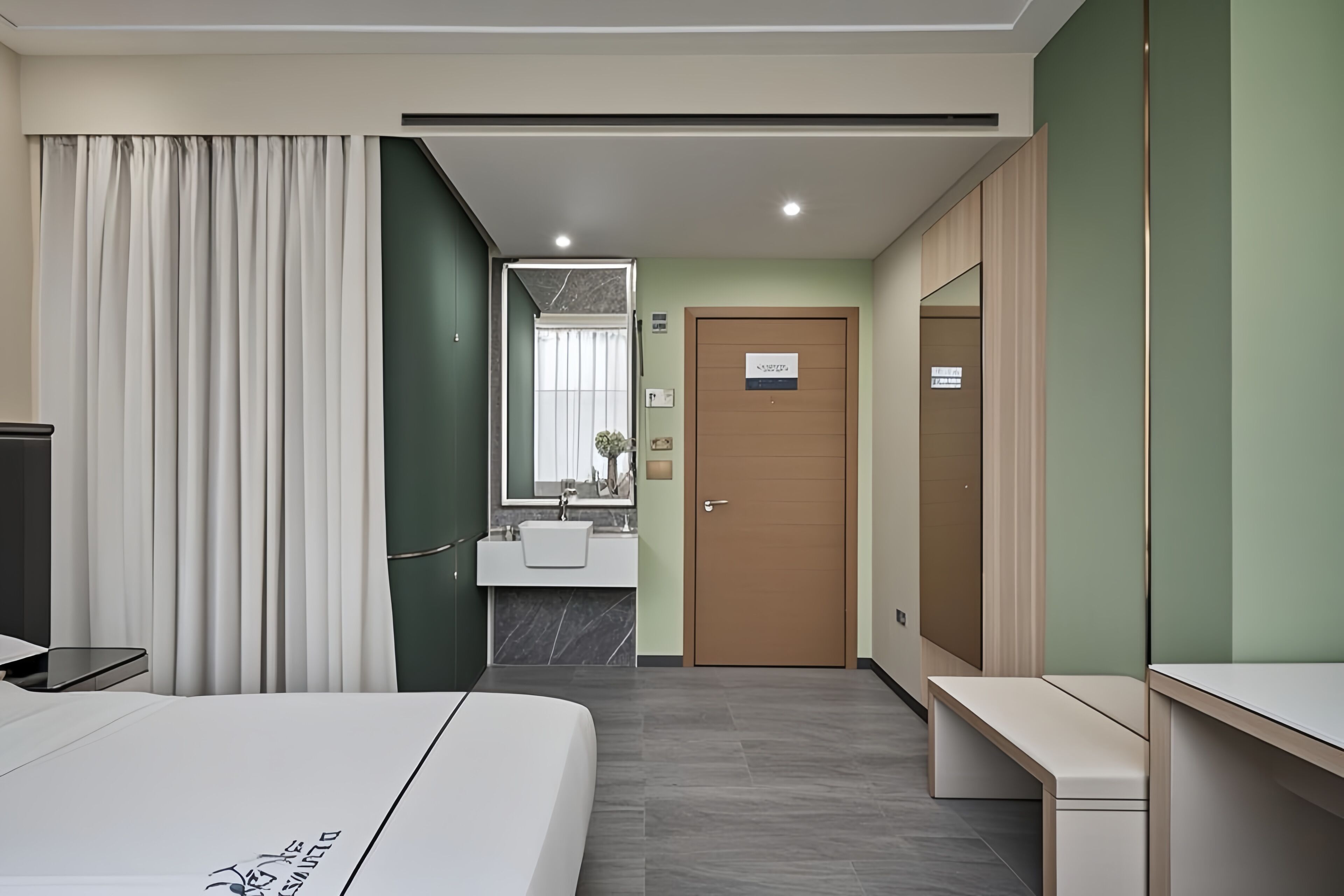 Une chambre d’hôtel moderne équipée d’un lit, d’un bureau, d’une salle de bain avec un lavabo et un miroir, et d’une porte.