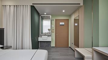 Une chambre d’hôtel moderne équipée d’un lit, d’un bureau, d’une salle de bain avec un lavabo et un miroir, et d’une porte.