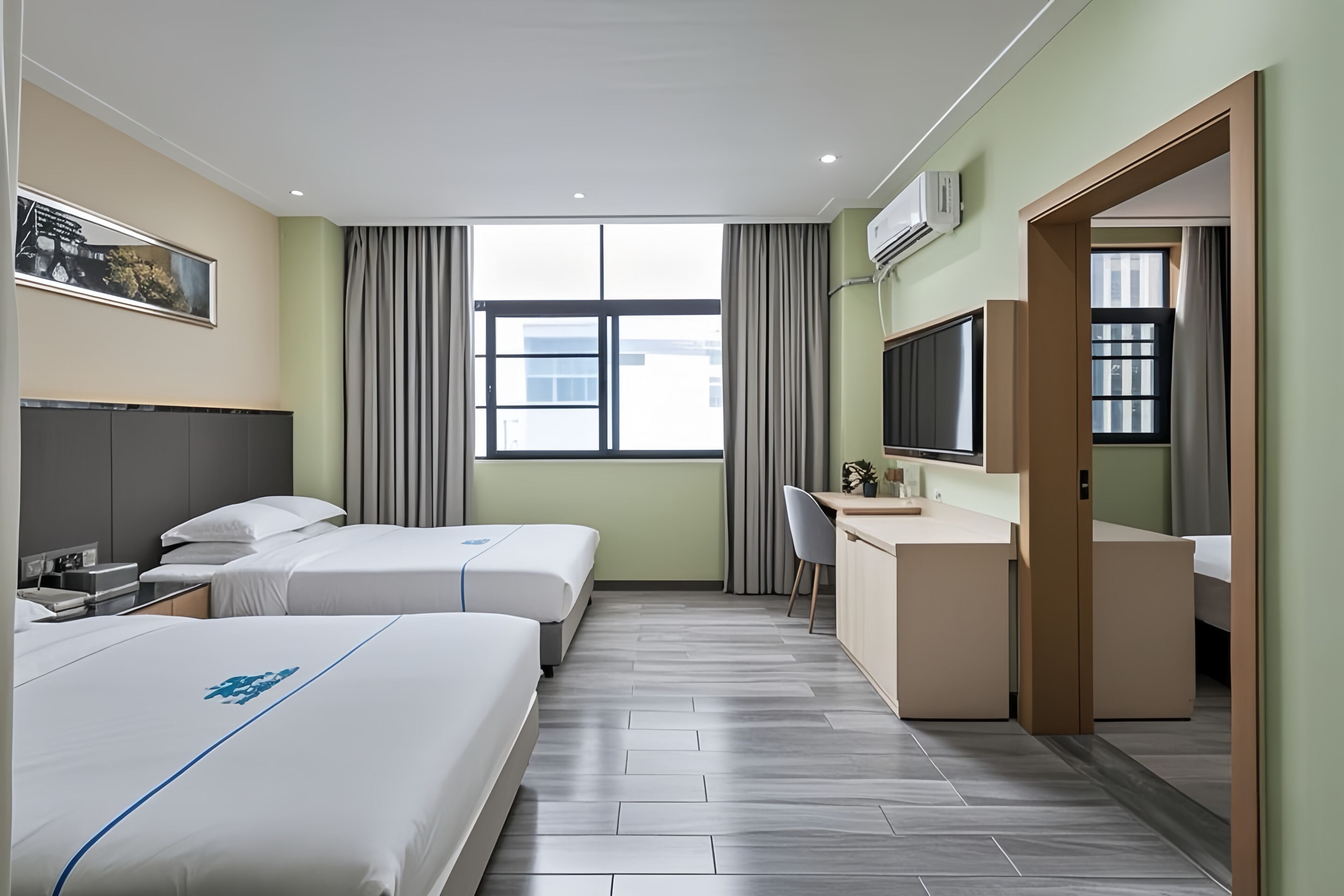 Habitación de hotel con dos camas, un escritorio, un televisor y un ventanal grande.
