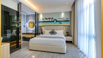A modern hotel room with a large bed, a glass-enclosed bathroom, a round mirror, and a wall mural.