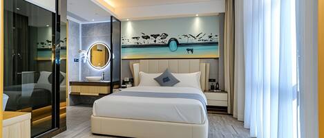 A modern hotel room with a large bed, a glass-enclosed bathroom, a round mirror, and a wall mural.