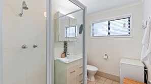 Ein Badezimmer mit Duschkabine, Toilette, Waschbecken und einem Fenster mit Jalousien.