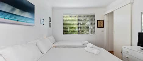 Habitación de hotel con dos camas, un ventanal con persianas, un cuadro en la pared y un televisor en una cómoda.