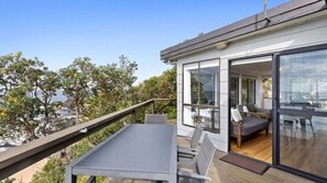 Eine moderne Terrasse im Freien mit Esstisch und Stühlen, mit Blick auf eine schöne Landschaft aus Bäumen und einem Gewässer.