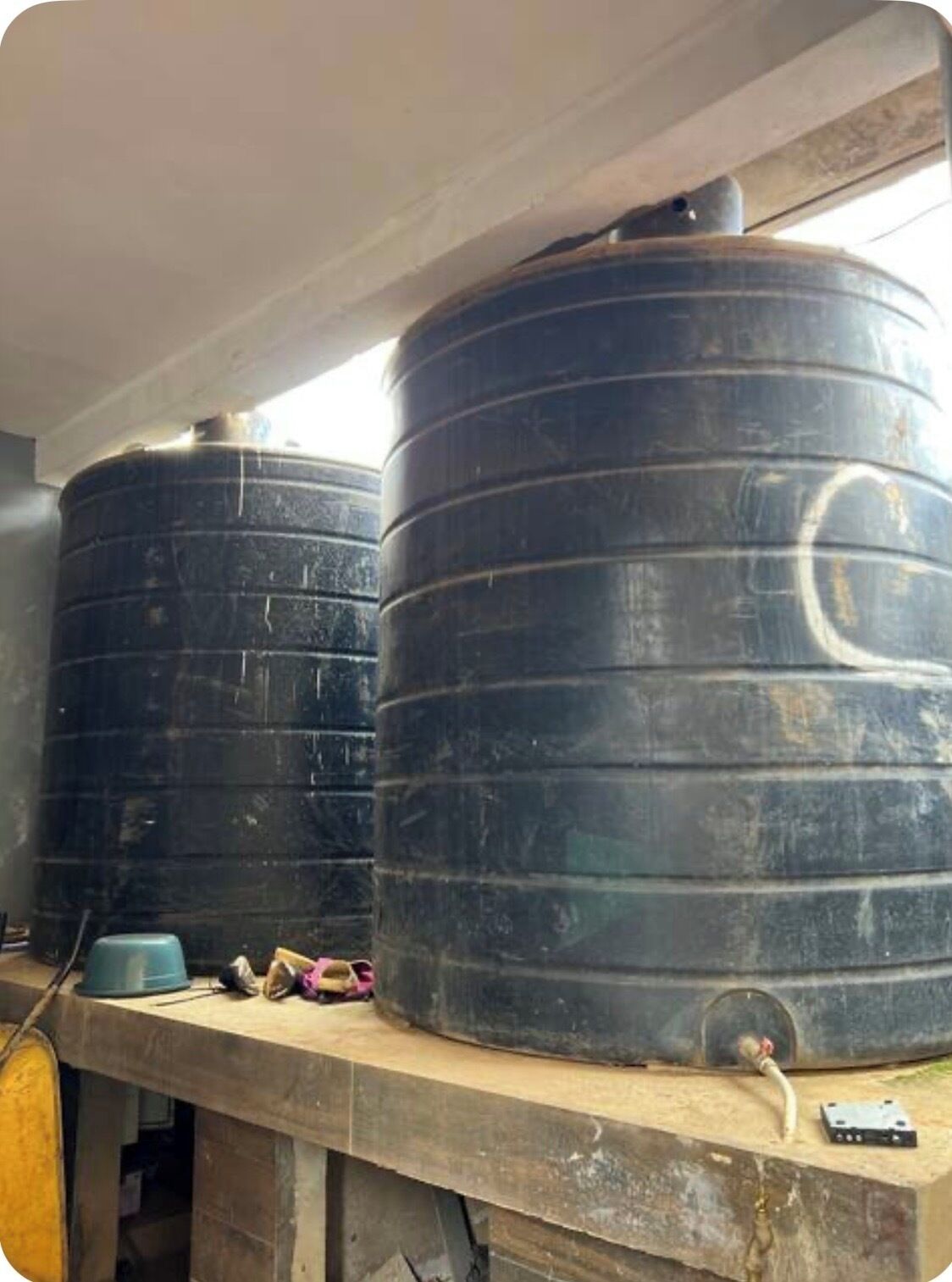 Two large black water tanks on a concrete platform with a hose connected to one.