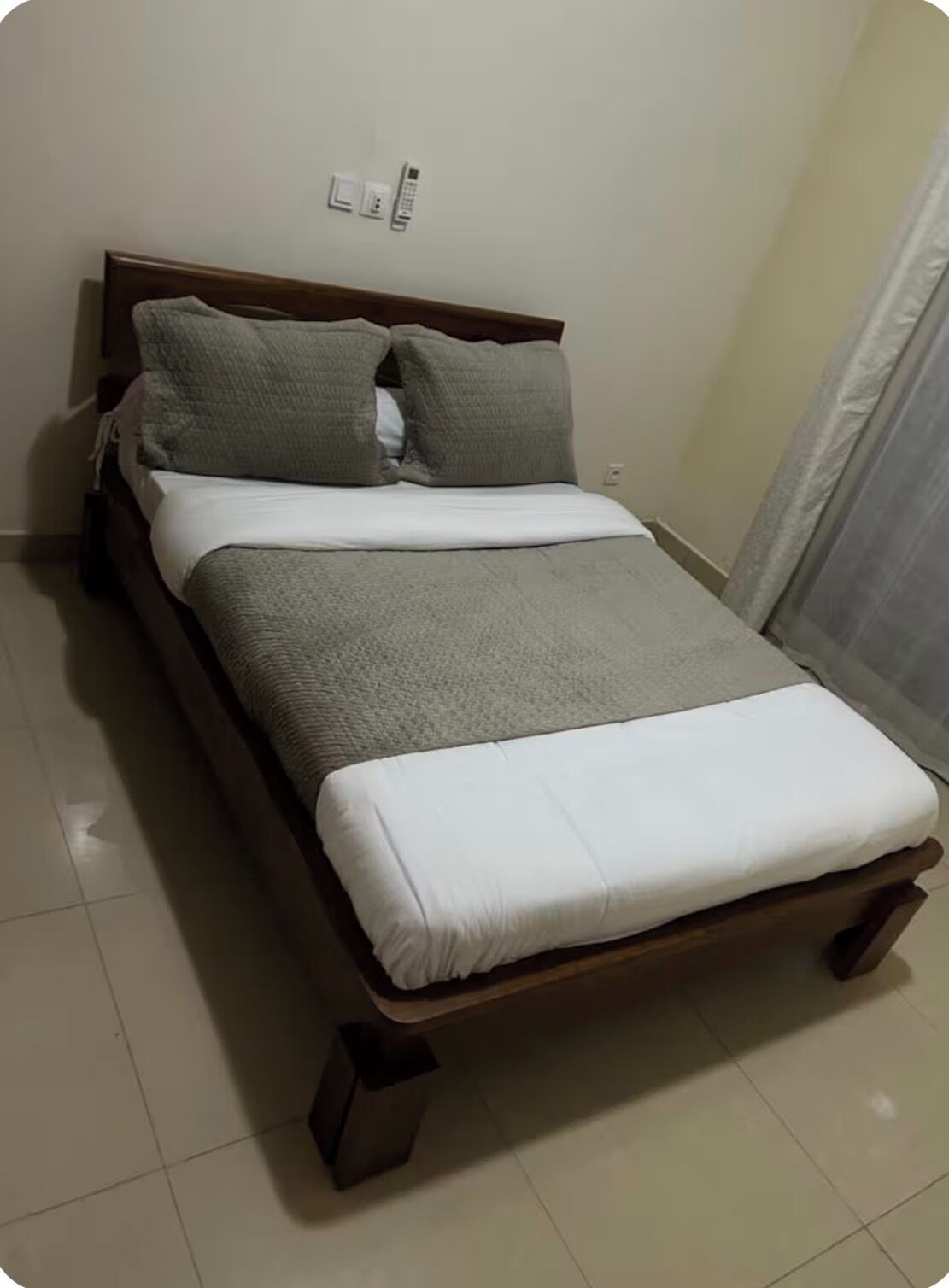 Una camera con un letto singolo, una cornice in legno, biancheria grigia e bianca e un comodino.