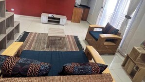 Un salon moderne avec un mur d’accent rouge, un téléviseur à écran plat, un ensemble de canapés, une table basse et un fauteuil en osier.