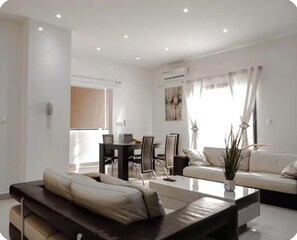 A modern living room with a sofa, coffee table, dining table, and chairs. - Résidence Hibiscus  (Yaoundé)