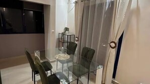 Un coin repas avec une table et des chaises en verre, une petite table d’appoint et un rideau.