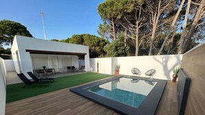 Un'area piscina moderna all'aperto con un solarium in legno, una piscina a sfioro e una zona salotto con sedie e tavolo.
