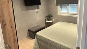 Una camera da letto moderna e accogliente con un letto, una TV a parete, un tavolino con una pianta e una finestra con persiane.