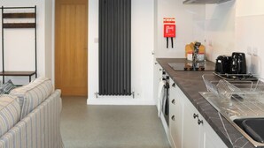 A modern kitchen with a built-in oven, a coffee maker, and a sink. There is a wooden door and a radiator on the wall. - 1 bedroom accommodation in Tregarth, near Bangor (Tregarth, near Bangor)