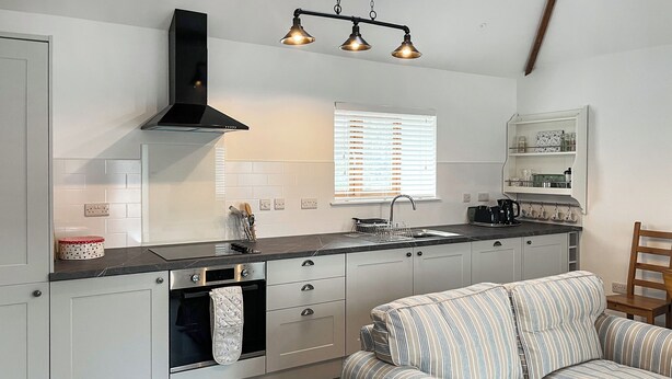 A modern kitchen with white cabinets, a black range hood, and a built-in oven. There is a striped sofa and a wooden chair in the living area. - 1 bedroom accommodation in Tregarth, near Bangor (Tregarth, near Bangor)