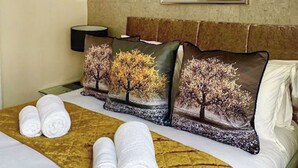 A hotel room with a bed, pillows with tree designs, a bedside lamp, and neatly folded towels. - Merewyke Boutique Apartment - UK51055 (Bowness-on-Windermere)