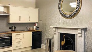 A modern kitchen with white cabinets, a built-in oven, and a dishwasher. There's a round mirror with a decorative frame above the fireplace. - Merewyke Boutique Apartment - UK51055 (Bowness-on-Windermere)
