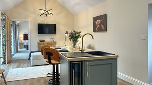 A modern kitchen with a central island, a dining area with a sofa and chairs, a TV mounted on the wall, and a chandelier. - 1 bedroom accommodation in East Stoke, near Newark (East Stoke, near Newark)