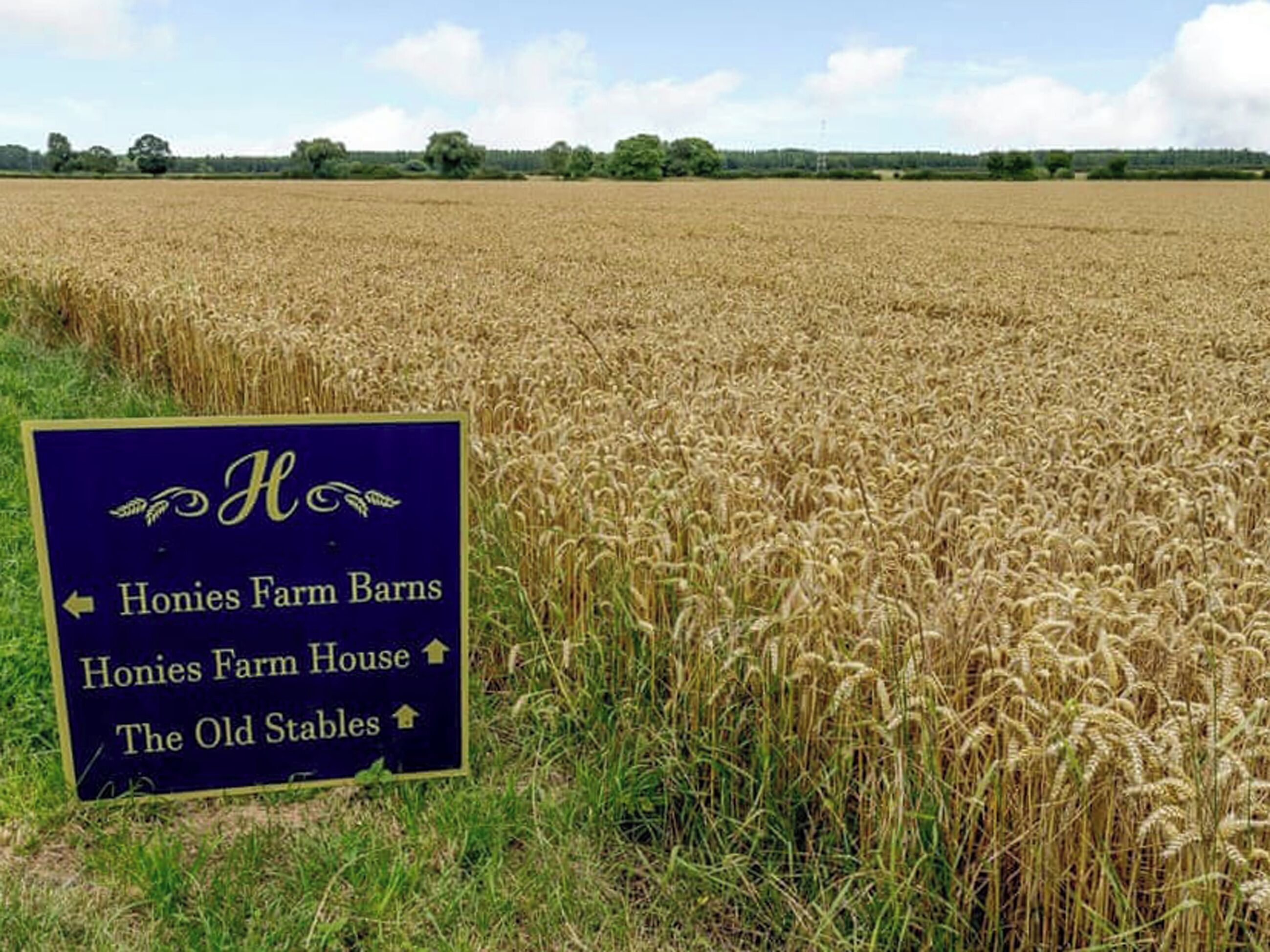 A sign in a field with directions to Honies Farm Barns, Honies Farm House, and The Old Stables.