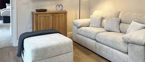 A living room with a sofa, ottoman, and a flat-screen TV mounted on the wall.