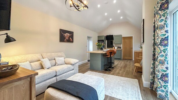 A modern living room with a sofa, ottoman, and a dining area with a bar. - 1 bedroom accommodation in East Stoke, near Newark (East Stoke, near Newark)