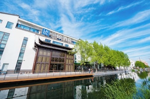 A traditional building with a large sign in the window, a reflection in the water, and a tree-lined pathway.