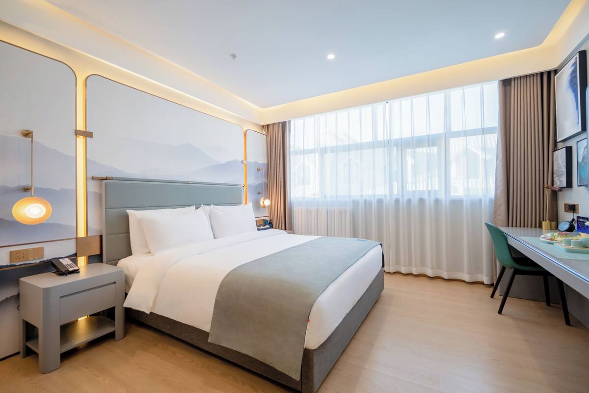 A hotel room with a large bed, a desk, and a view of mountains through the window.