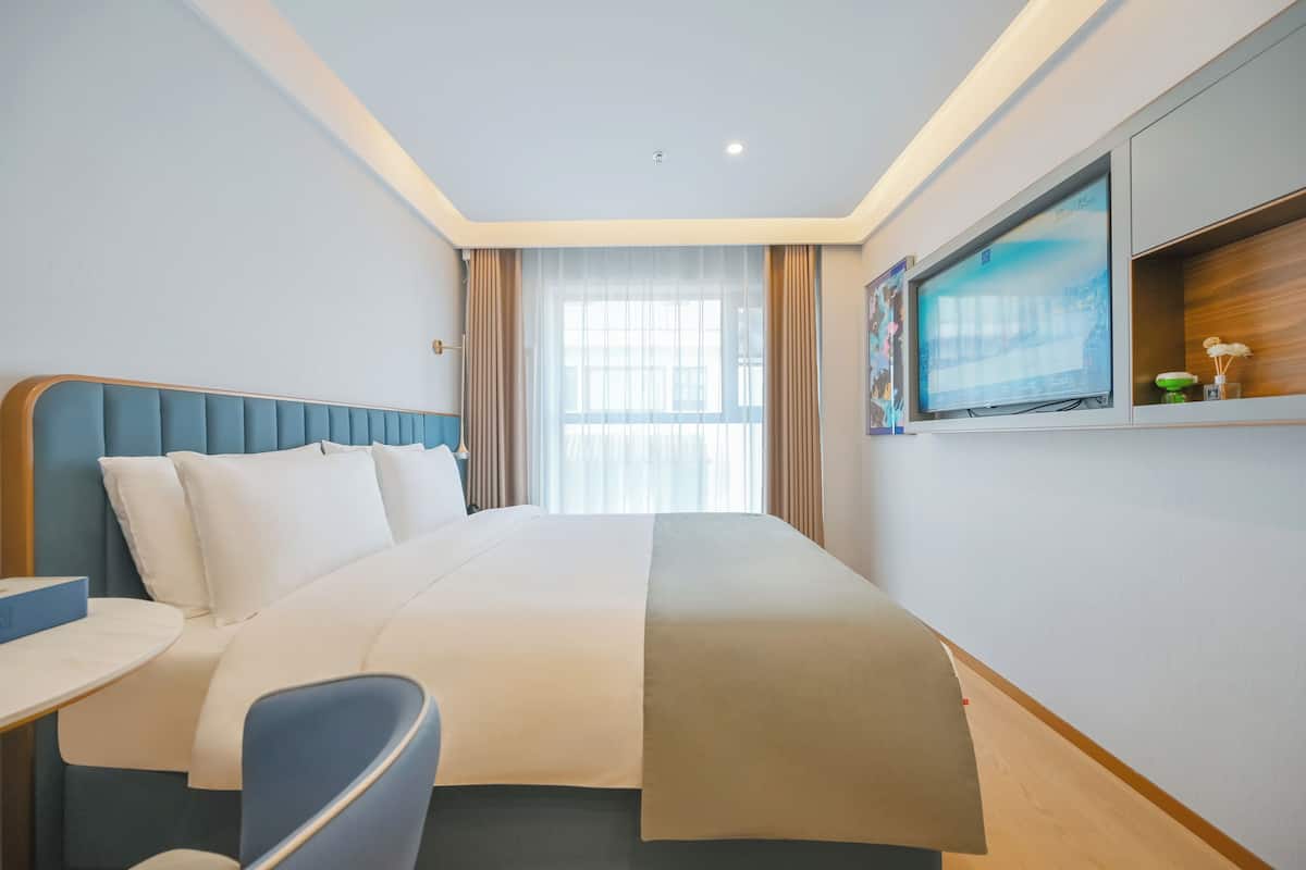 A hotel room with a large bed, a desk, a chair, a television, and a window with curtains.