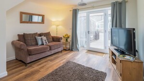 Een woonkamer met een bank, een televisie, een lamp en uitzicht op buiten.