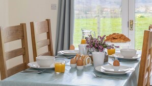 Een ontbijttafel gedekt met borden, bekers, een karaf sinaasappelsap, eieren, croissants en een vaas bloemen.