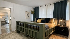 Un dormitorio con cama, mesita de noche, planta colgante y vistas al pasillo.