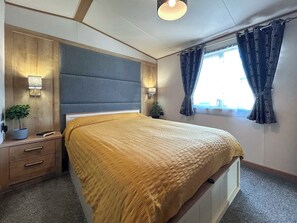Un dormitorio con cama, mesitas de noche, lámpara, ventana con cortinas y vista al cielo.
