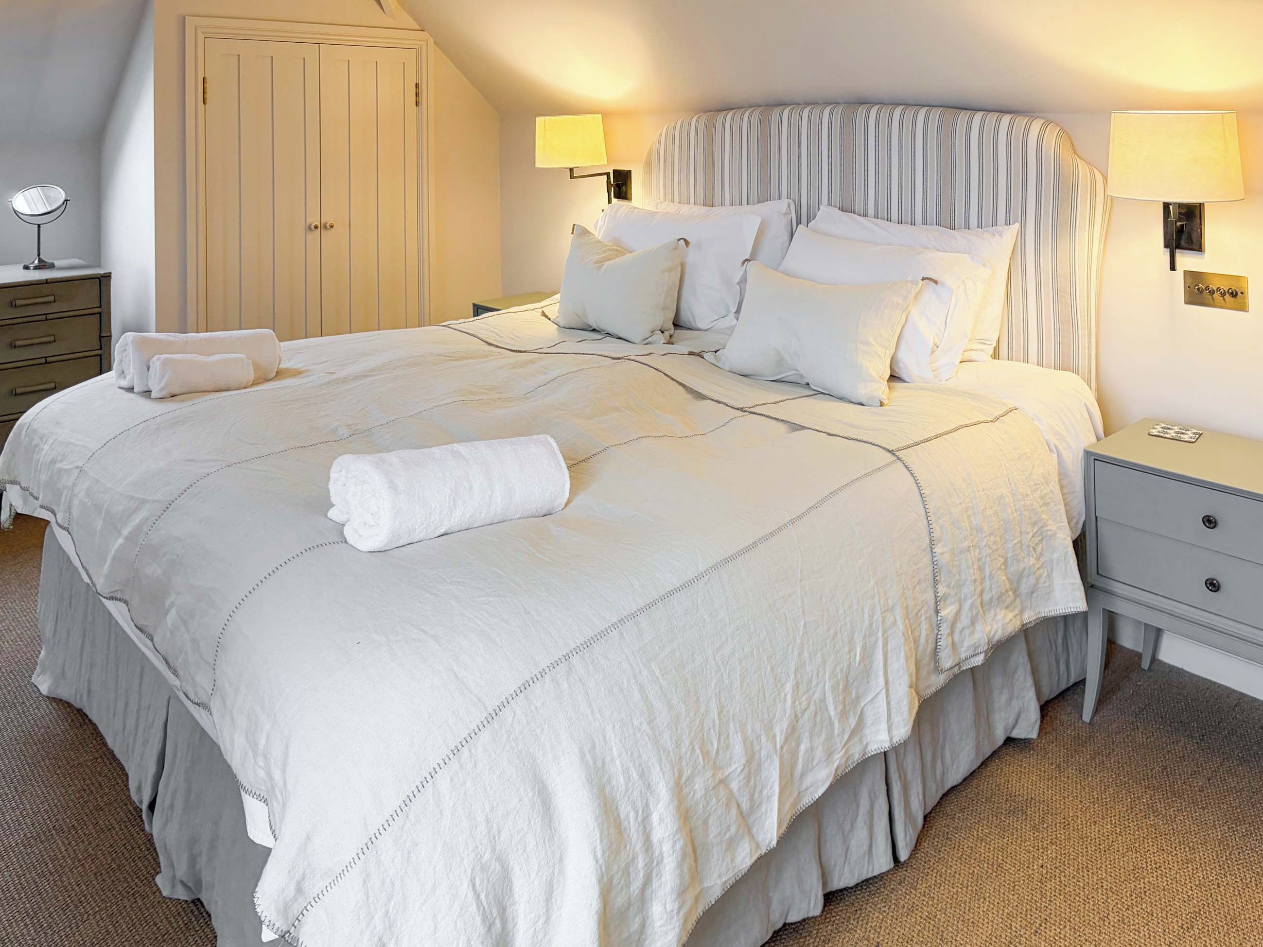 A neatly made bed with a striped headboard, two bedside lamps, a small bedside table, and a wardrobe.
