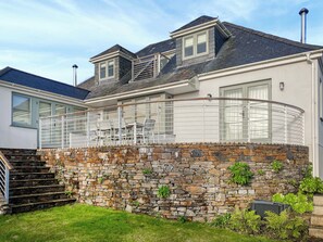 A house with a stone wall, a balcony with metal railings, and a staircase leading to the entrance.