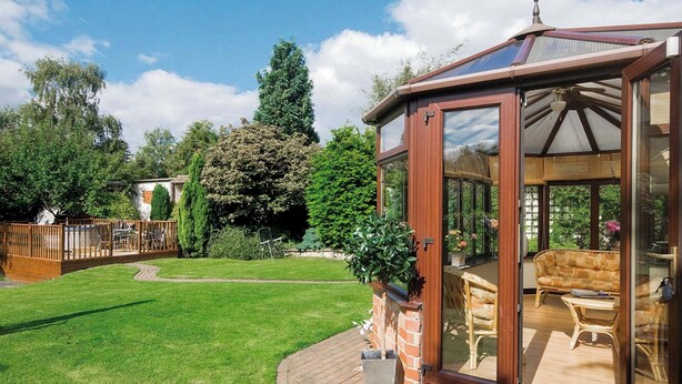 Une véranda dotée d’une porte vitrée, d’une terrasse en bois et donnant sur le jardin.