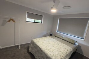 A bedroom with a bed, a ceiling fan, a window with a blind, and a radiator.