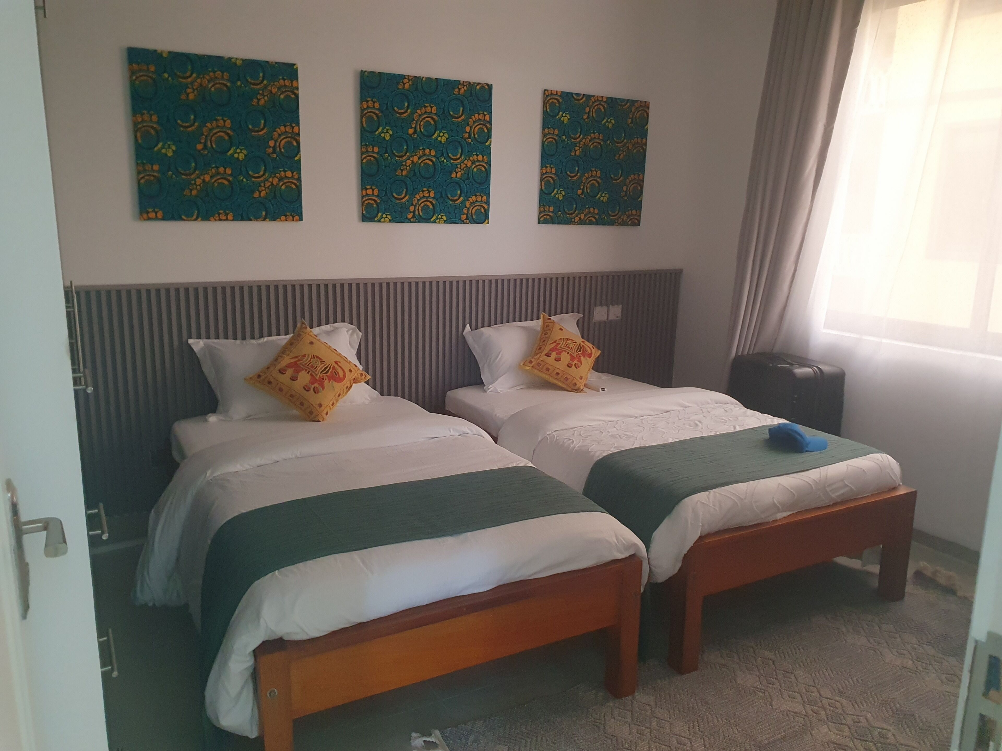 Een hotelkamer met twee bedden, een houten hoofdeinde en een raam met gordijnen.