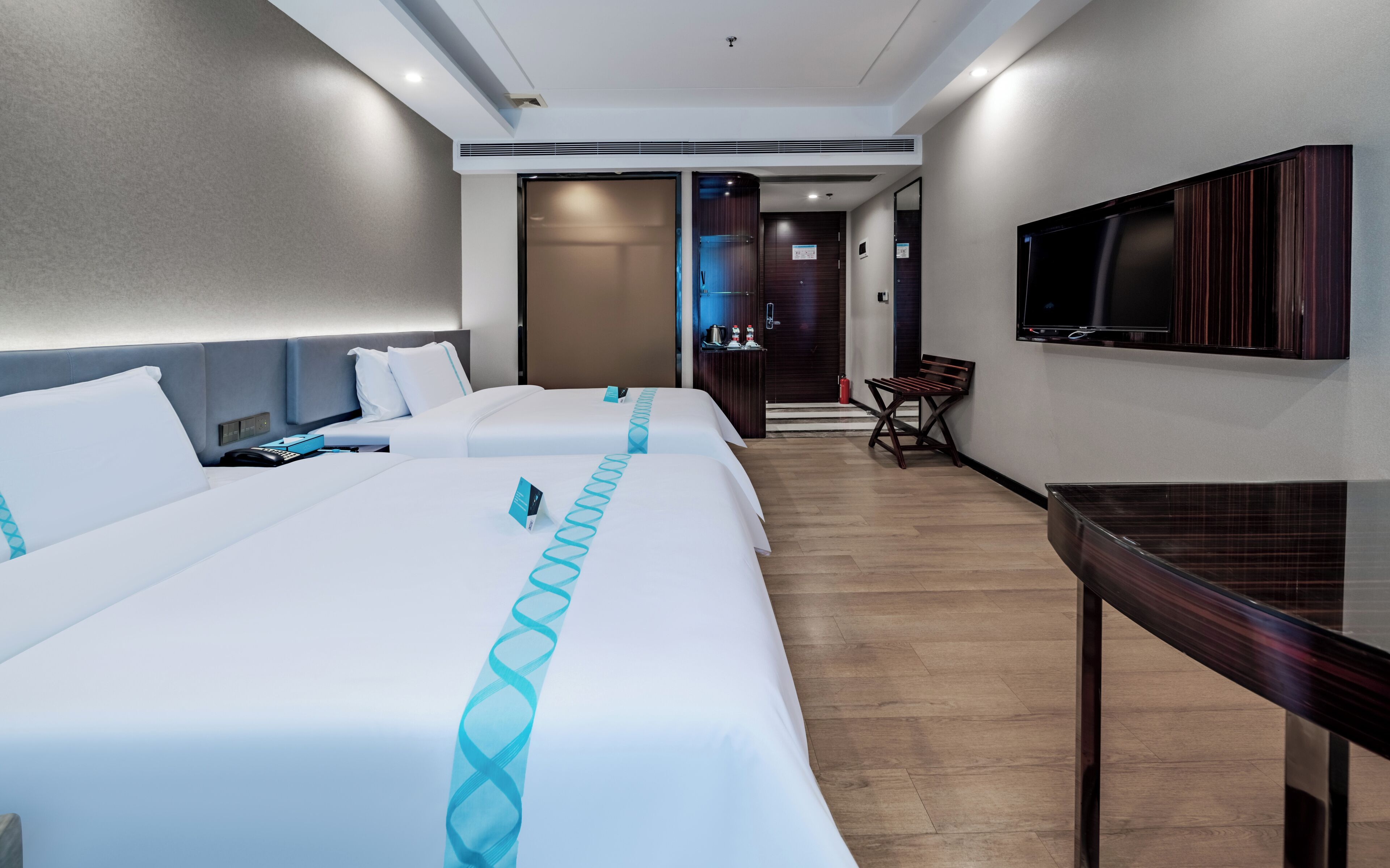 A hotel room with two beds, a TV, a desk, and a chair.